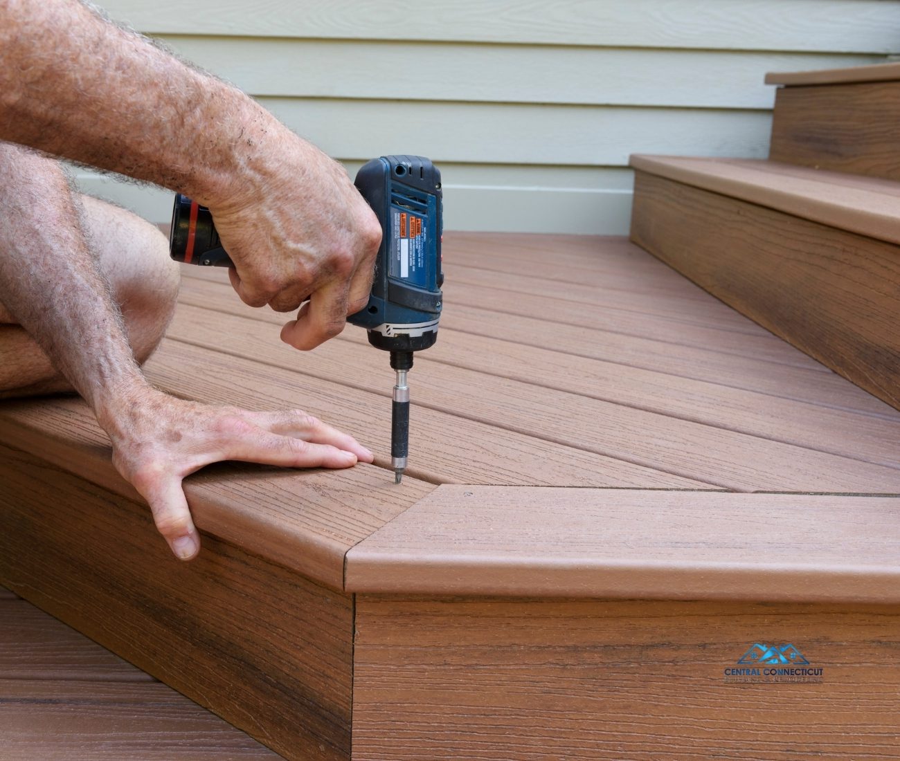 Deck Build in Berlin Close-up of a contractor’s hands using a power drill to secure composite decking boards during the construction of a new deck in Berlin, CT — built by Central Connecticut Building & Remodeling.