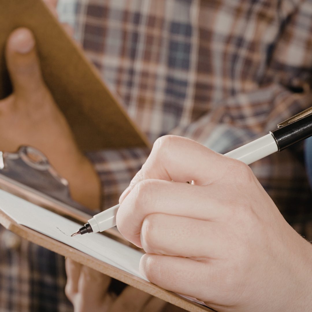 Person holding a clipboard and writing notes while inspecting storm damage, documenting repairs and damages for insurance purposes.